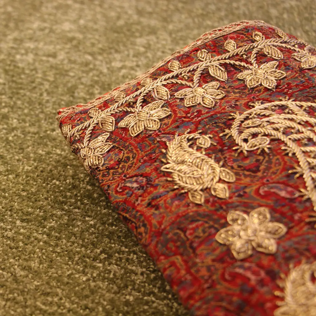 نمای نزدیک از پارچه سنتی ایرانی با ترمه دوزی طلایی روی زمینه موکت تافتینگ سبز